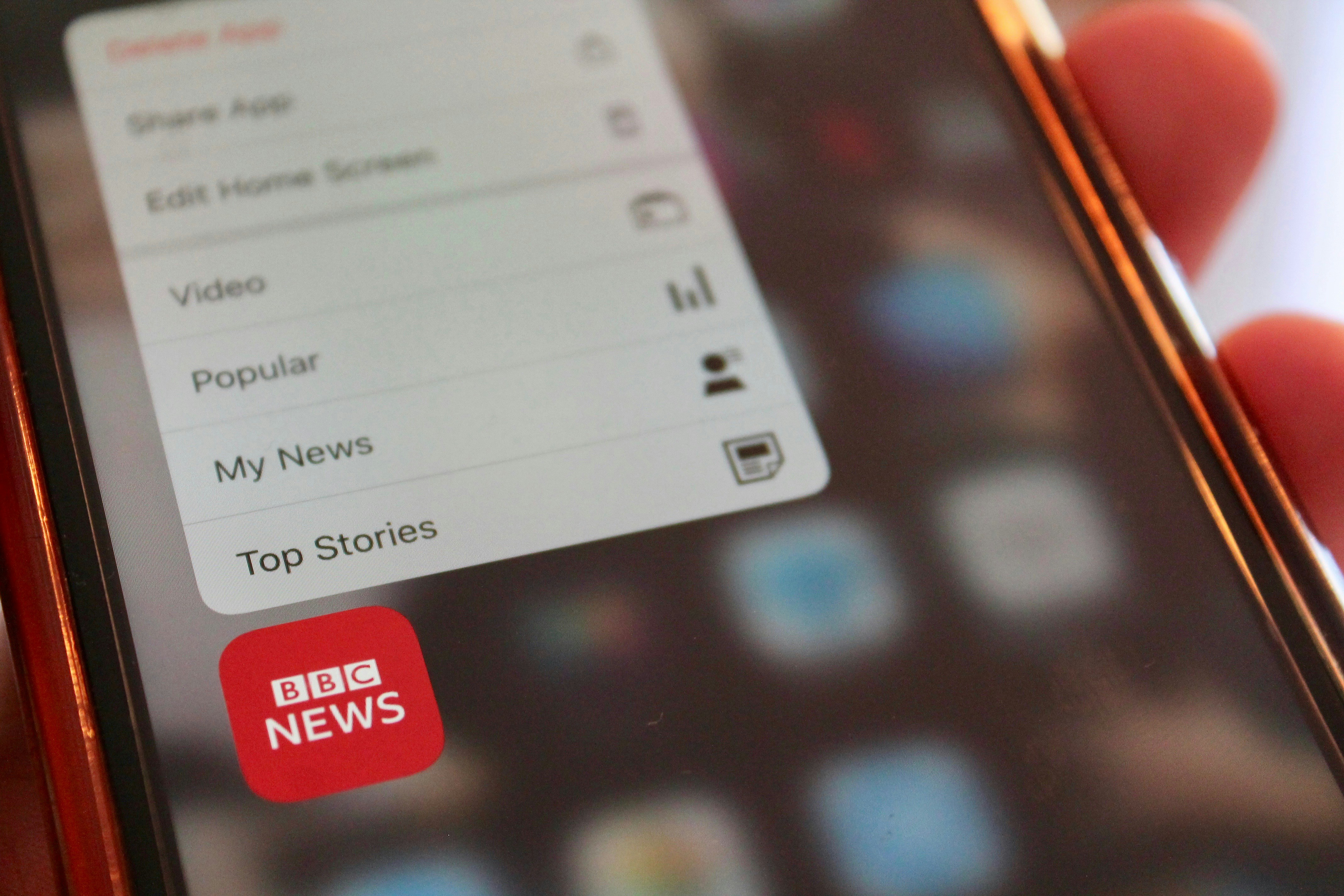 Close-up of a smartphone screen displaying the BBC News app icon with quick access menu options like “Top Stories” and “My News,” symbolizing the digital reach and editorial influence of the British Broadcasting Corporation.