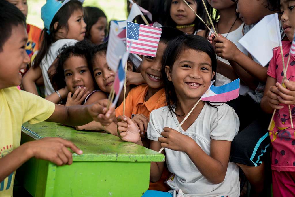 Filipino children smiling and waving U.S. and Philippine flags during a community event
