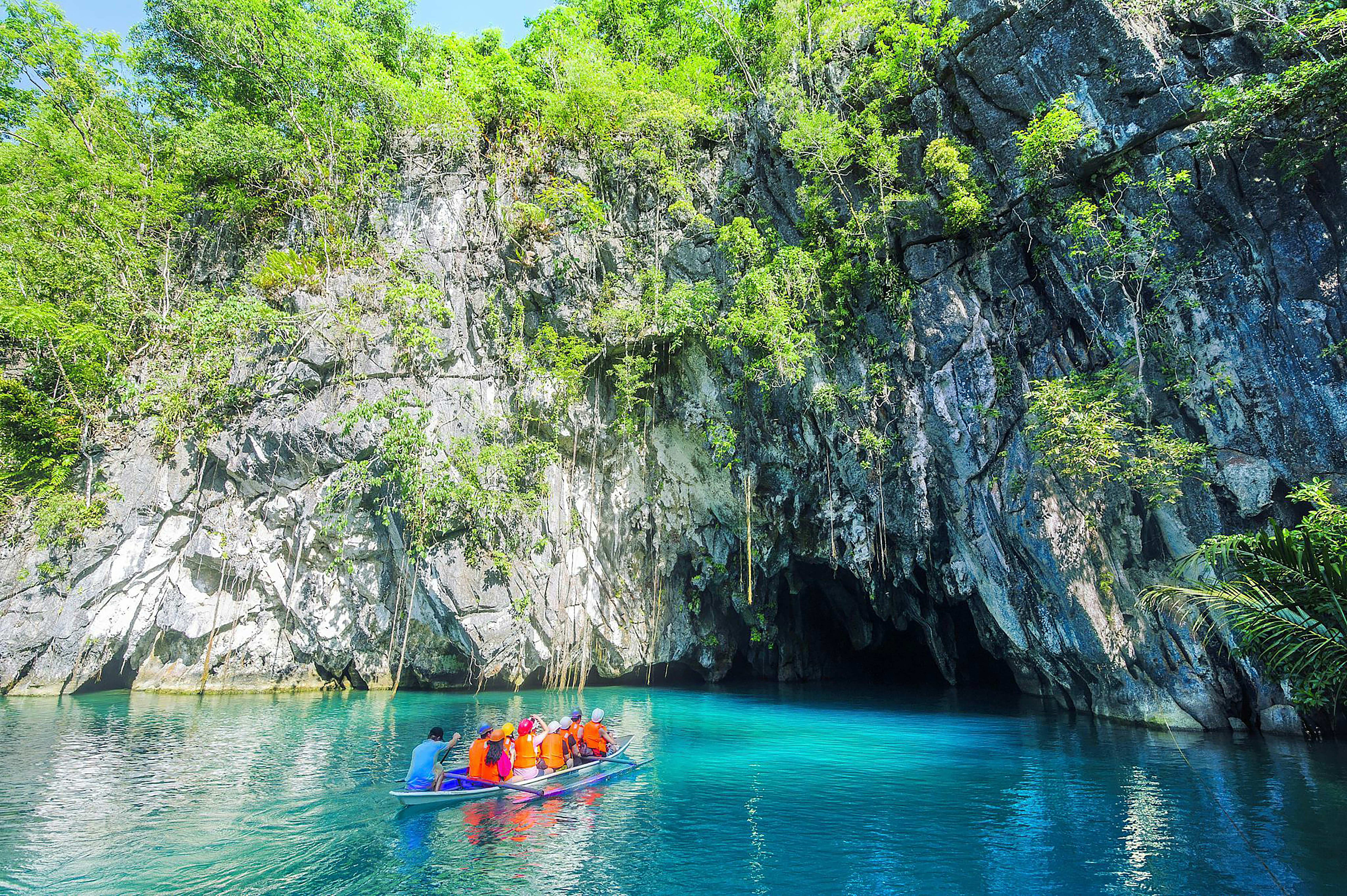 Tourists on a paddleboat entering the Puerto Princesa Underground River cave, surrounded by limestone cliffs and turquoise water in Palawan, Philippines.