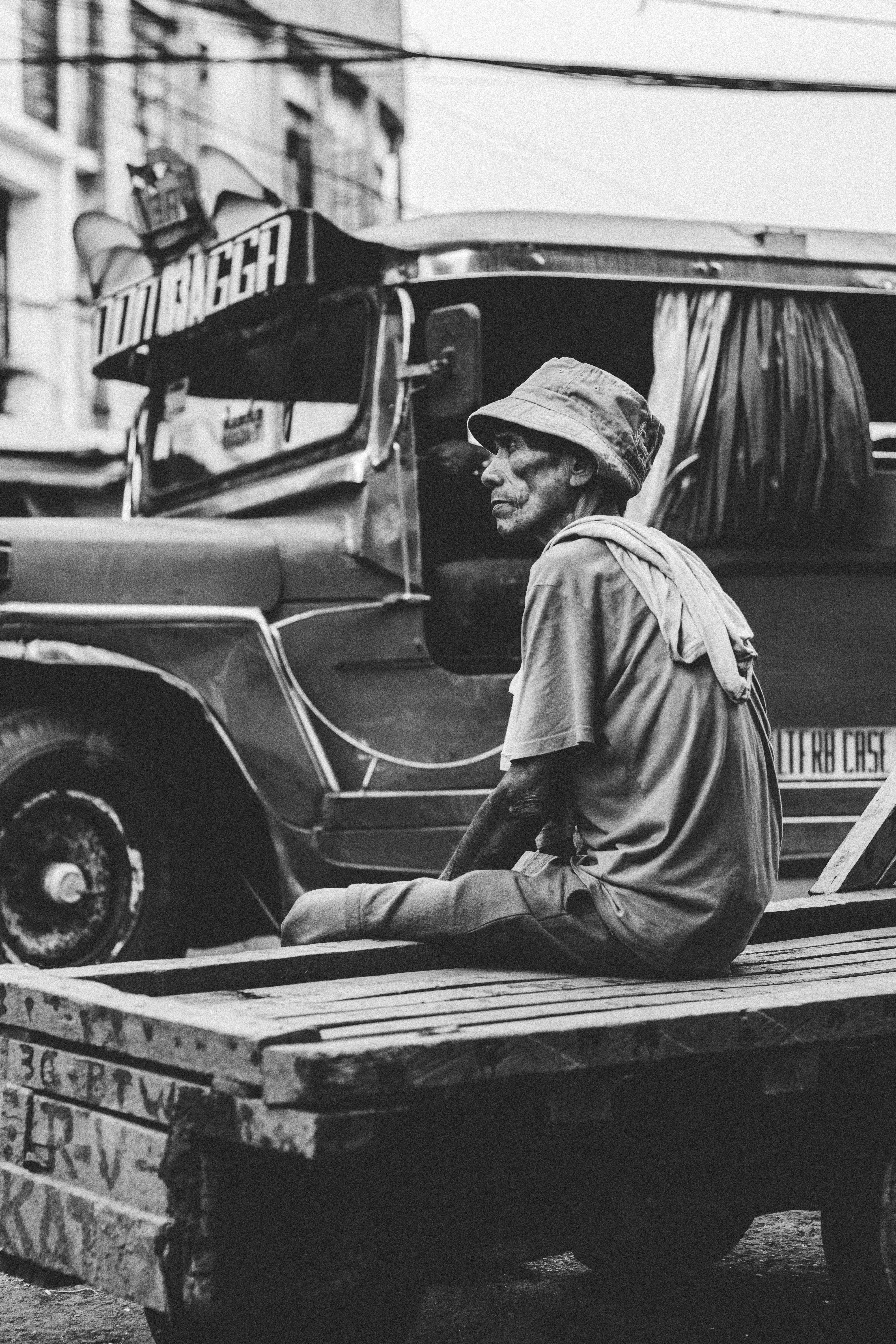Black-and-white photo of an elderly Filipino man sitting on a wooden cart beside a jeepney, capturing the raw street-level realities of life under Duterte’s presidency and the socioeconomic struggles often overshadowed by his rhetoric.